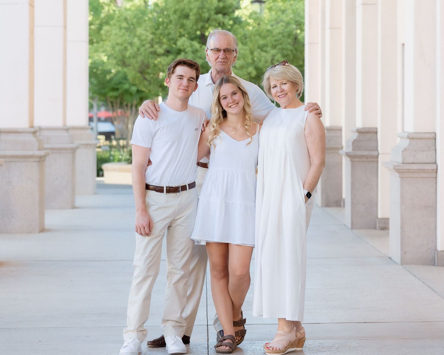 Family of four posing in white outfits under elegant columns outdoors.