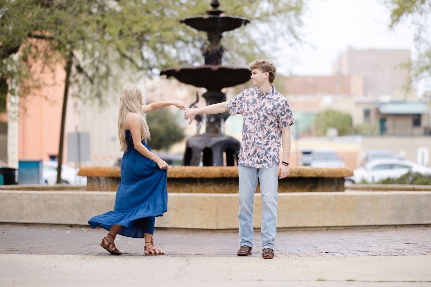 A couple dances together near a decorative fountain in an outdoor plaza setting.