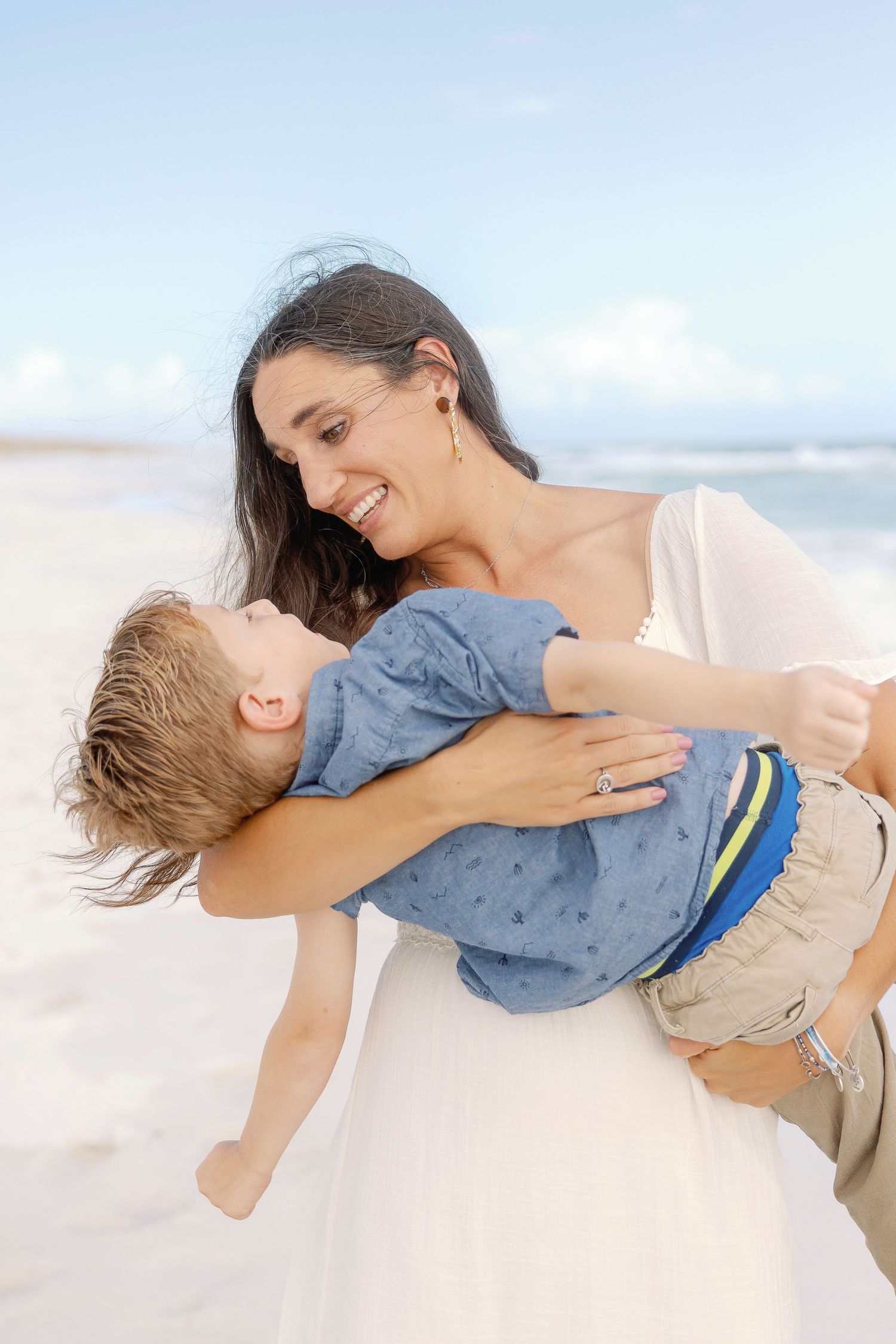 Mother and child sharing playful embraces and tender moments on a sunny beach.