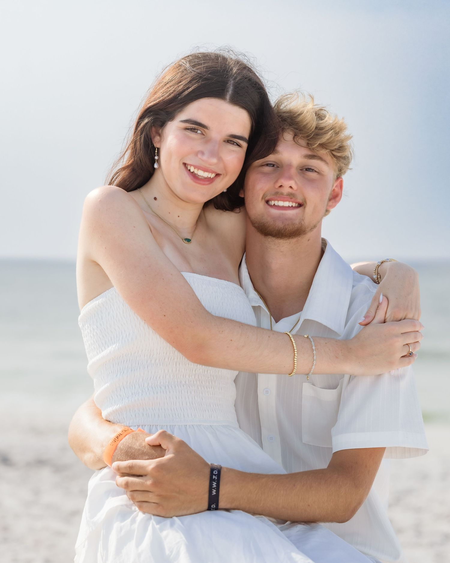 Happy young couple embracing and smiling together on a sunny white sand beach.