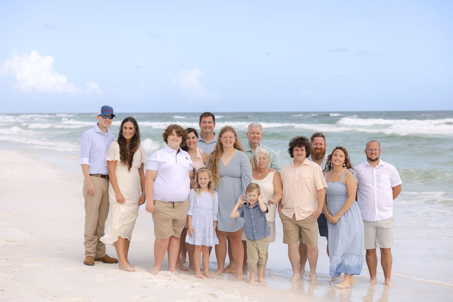 Large family group posing together on a sunny beach with turquoise ocean waves in the background.
