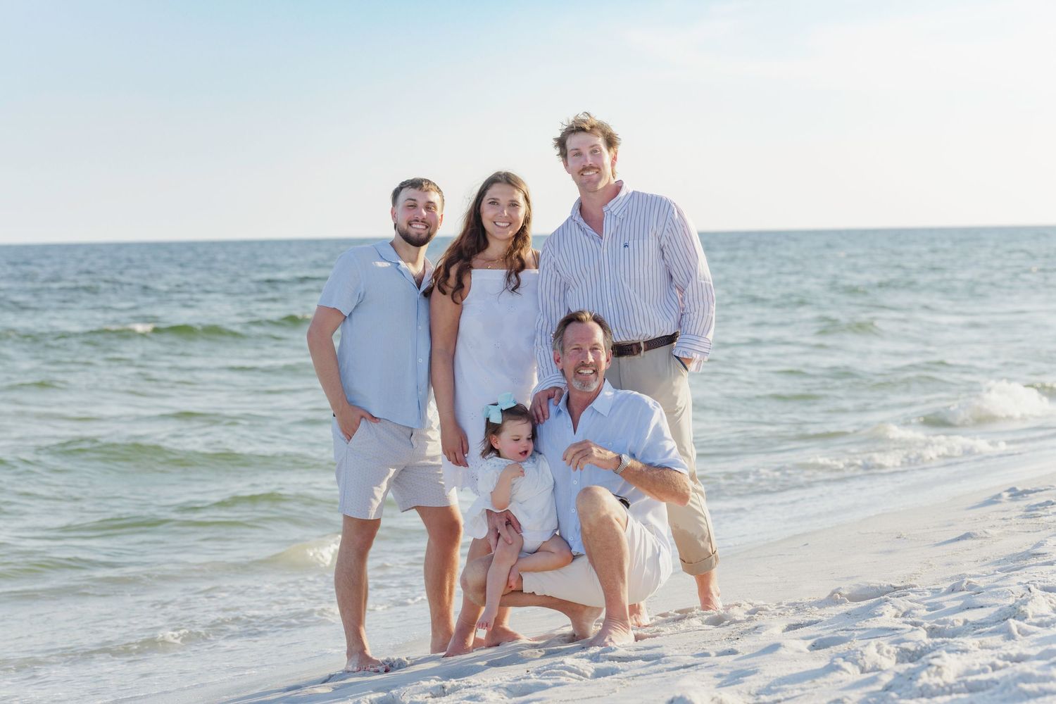 Happy family of five poses together on a white sand beach on a sunny day.