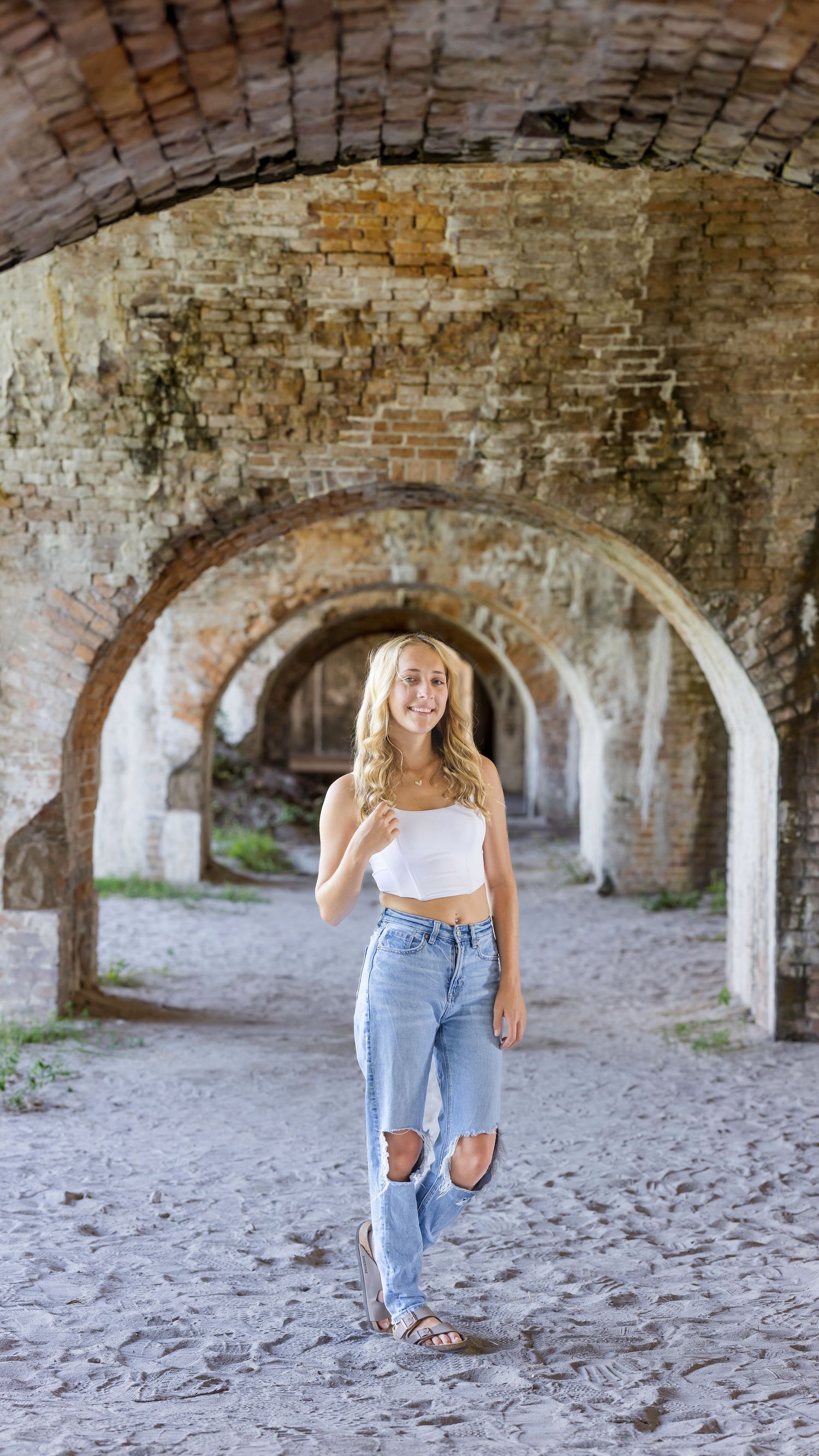 A casual summer outfit featuring distressed jeans and white crop top photographed under historic brick archways.