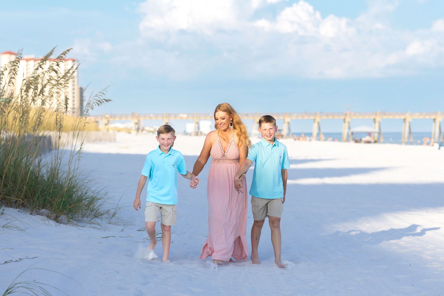 A family poses for a beach photo with sea oats and white sand dunes in the background.