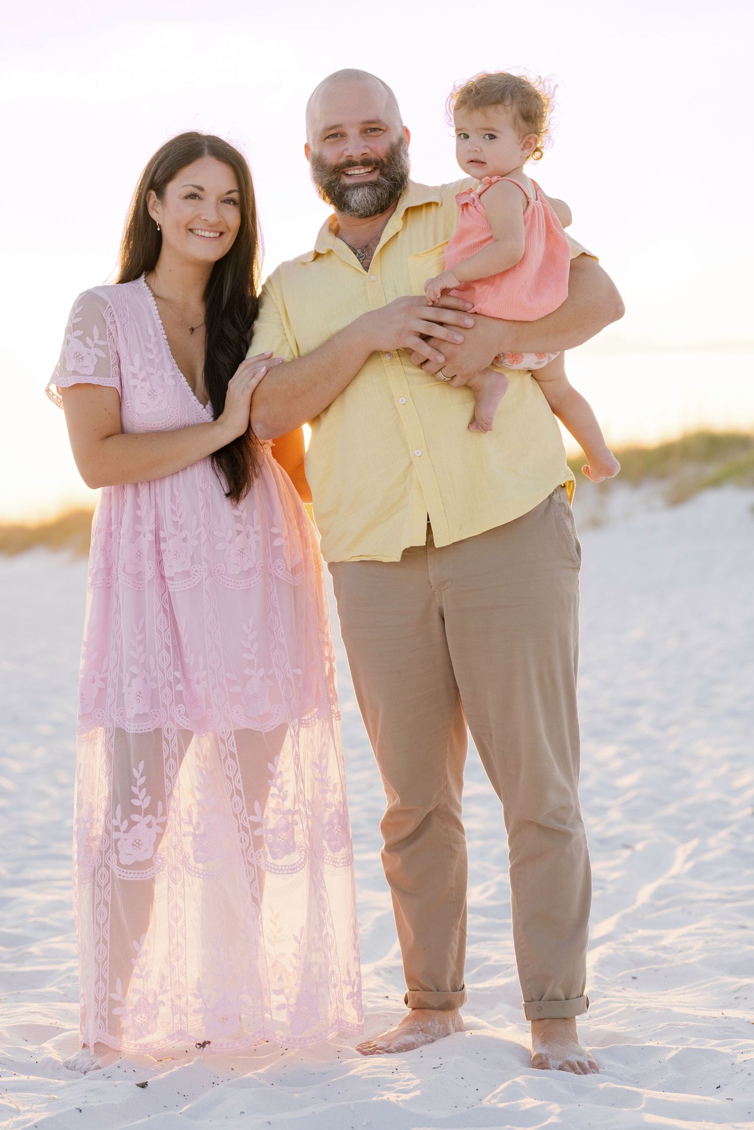 A family poses together on a beach wearing coordinating pink and yellow outfits at sunset.