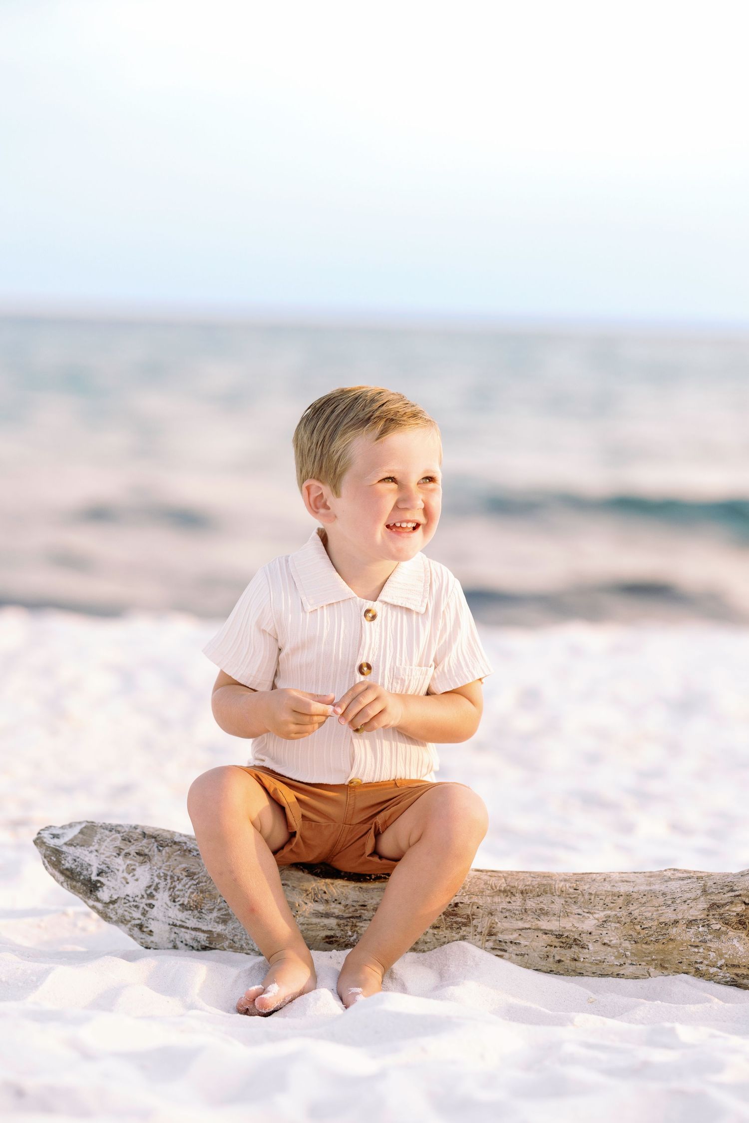 A small child plays joyfully on a pristine white sand beach wearing brown shorts and a light colored top.