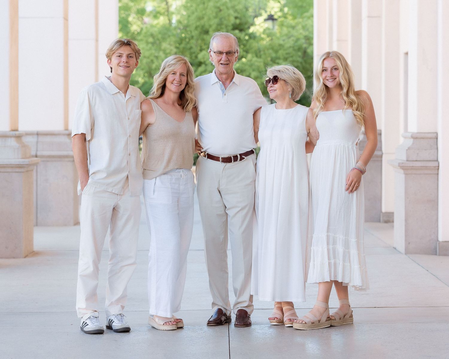 Family of five posing together in coordinated white and neutral outfits between elegant columns outdoors.