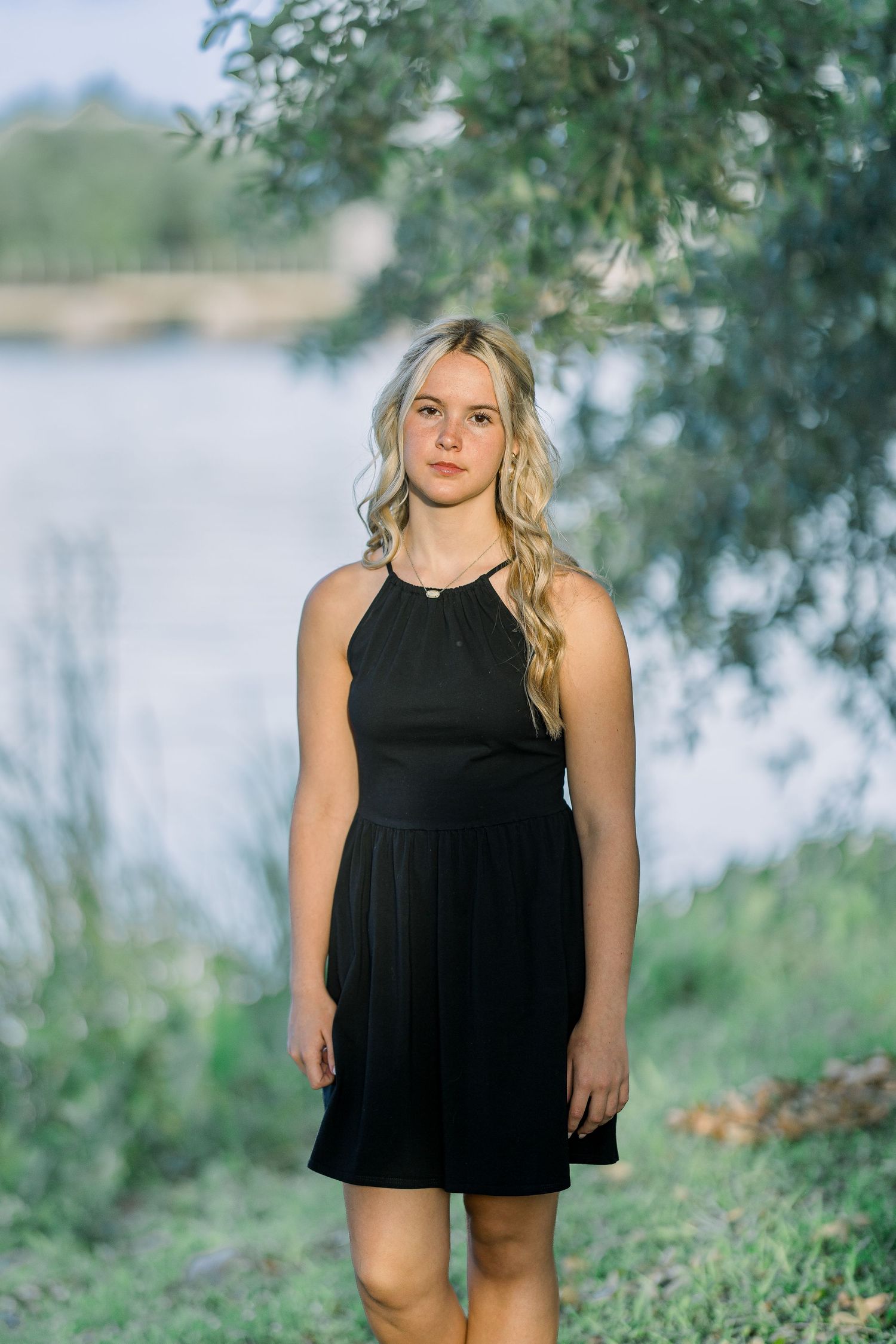 Lifestyle portrait featuring a black dress against a lakeside setting with trees.