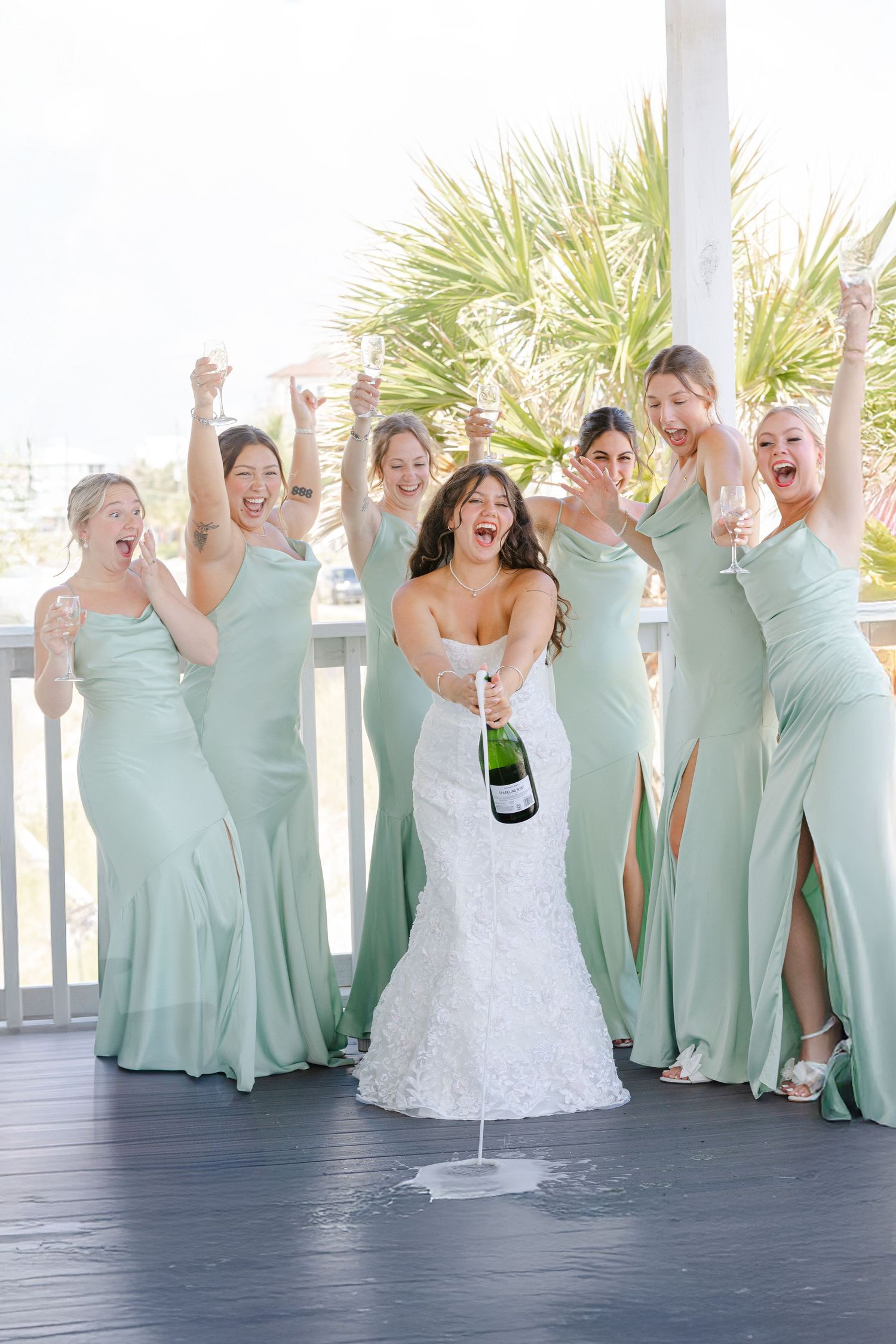 Wedding party cheers with champagne while wearing coordinated mint green and white dresses.