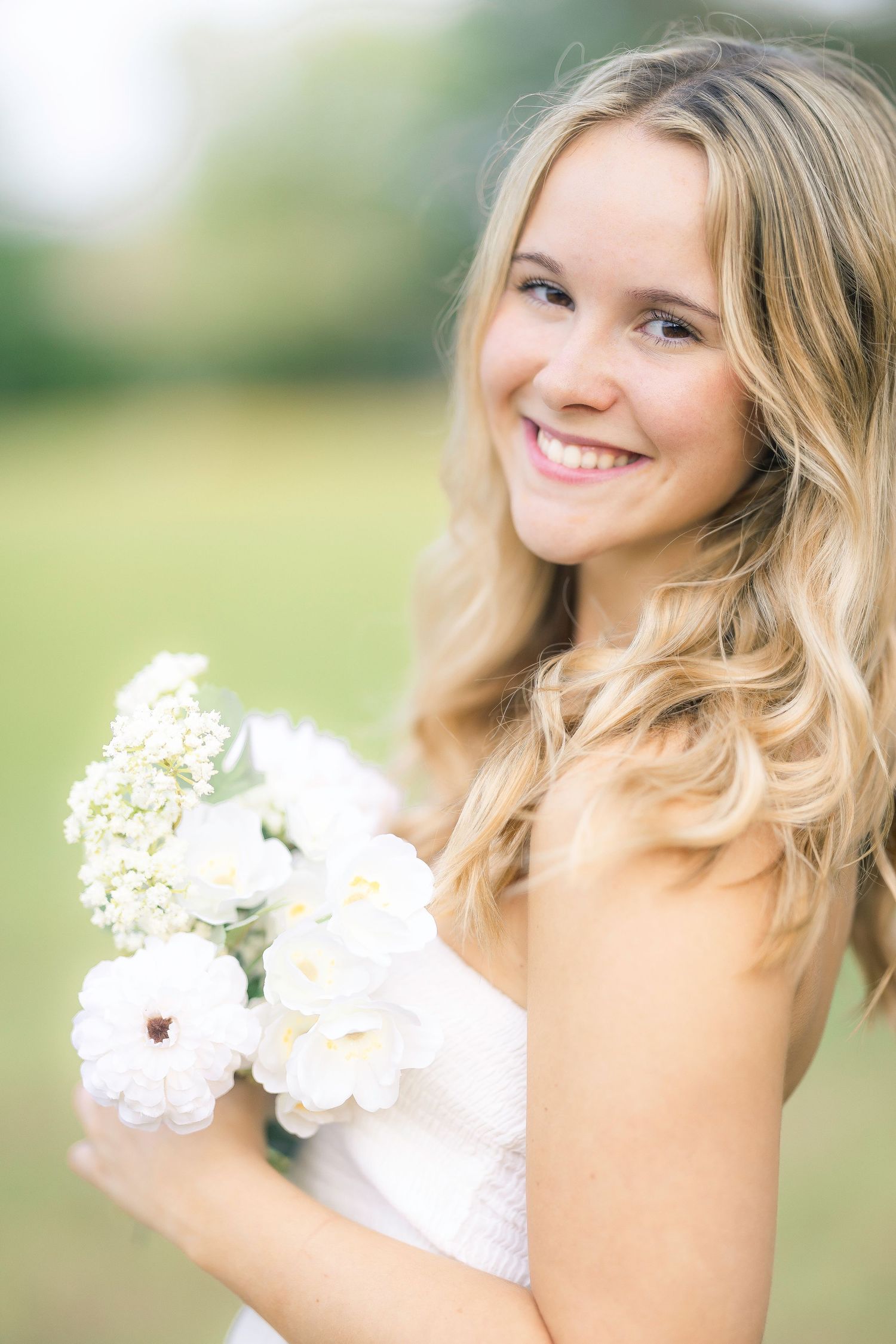Smiling blonde bride holding white flower bouquet in elegant outdoor portrait.