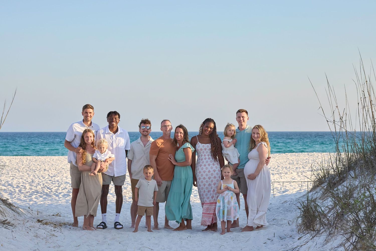 Large family group portrait on a white sand beach with turquoise ocean water in the background on a sunny day.