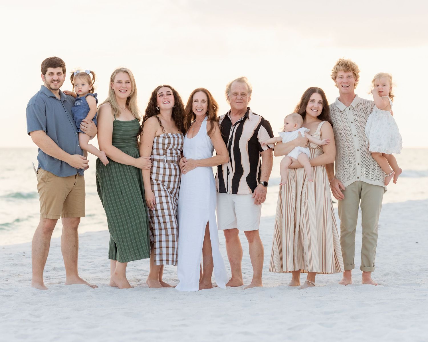 Large family group portrait smiling together on sandy beach near ocean shore.