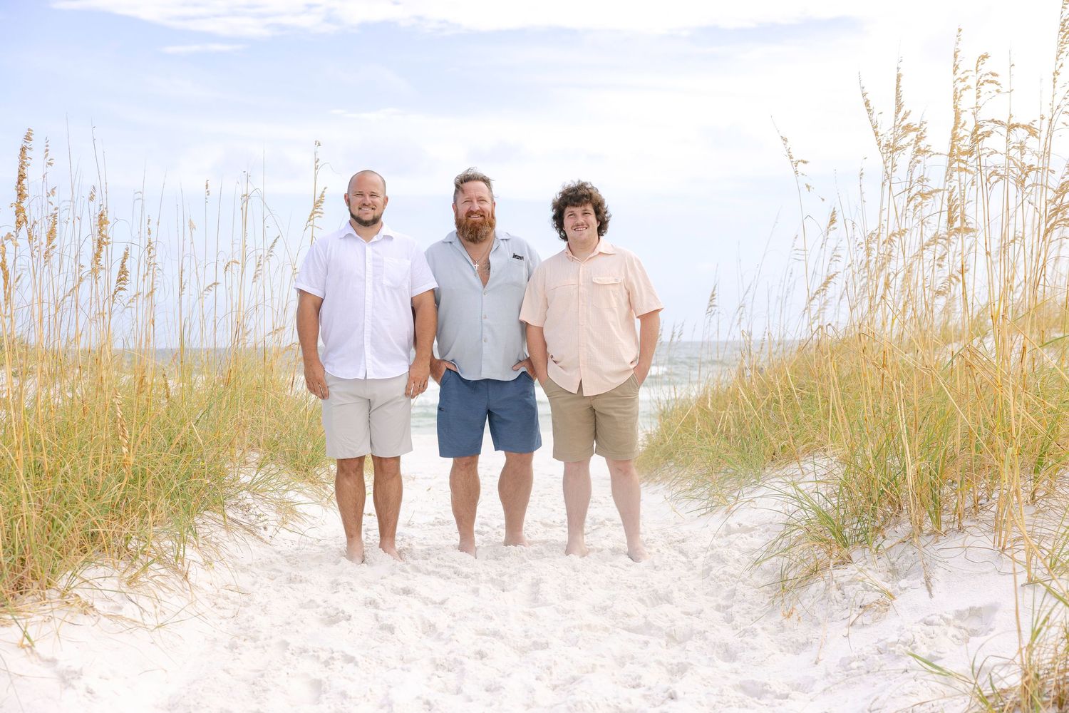 Family members walking together on a sandy beach path through sea oats on a sunny day.