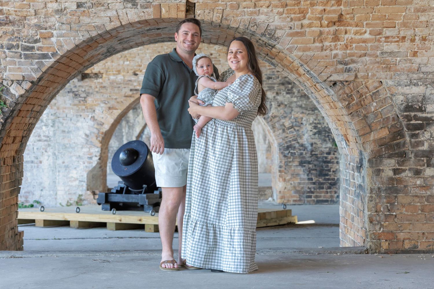 Family of three posing under brick arches with a historic cannon at a Civil War era fort.