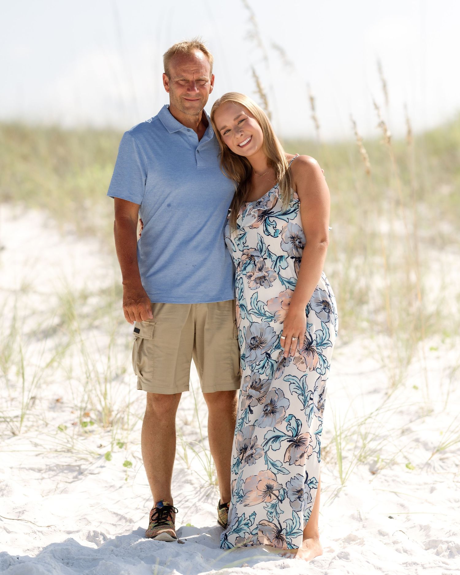 Happy couple posing together on white sand beach dunes with sea oats.