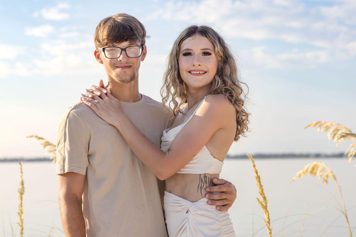 Joyful couple embraces and smiles together during sunset photoshoot at the beach.