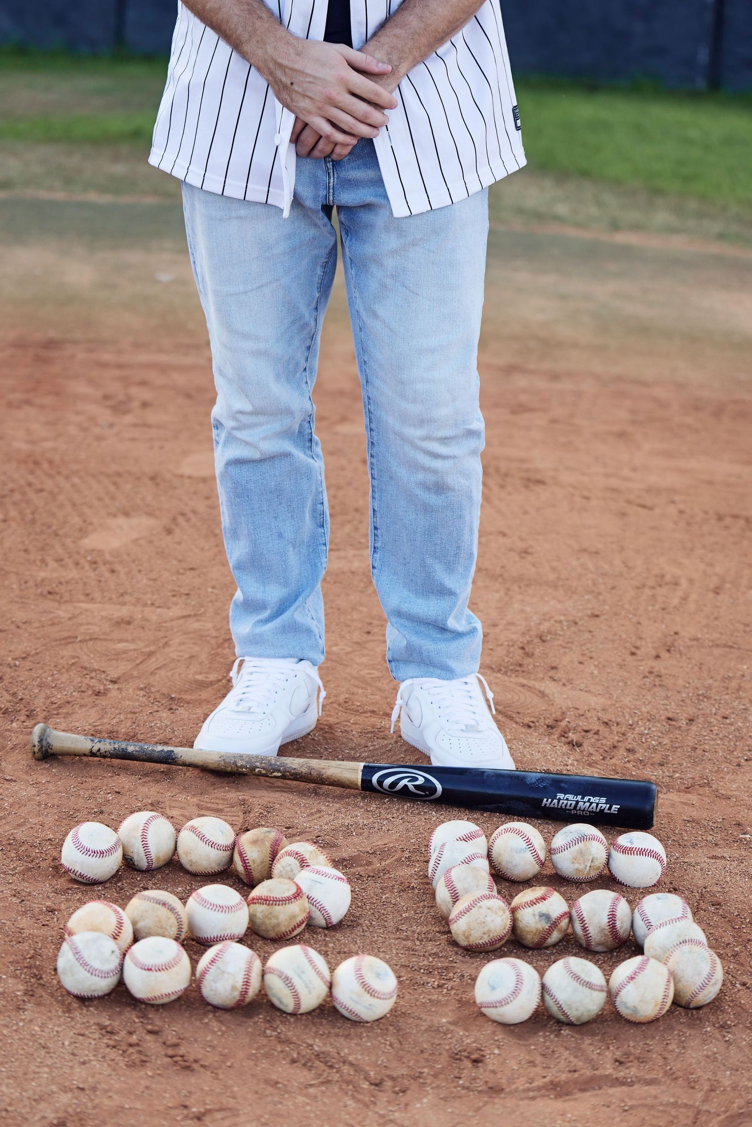Baseballs arranged in numbers from 1 to 5 on a dirt baseball field with a baseball bat and pinstripe uniform visible.