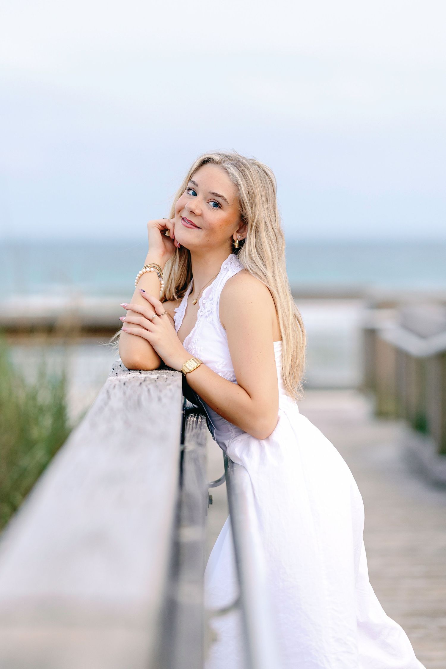 Artistic portraits on a coastal boardwalk with someone in white leaning against the railing at sunset.