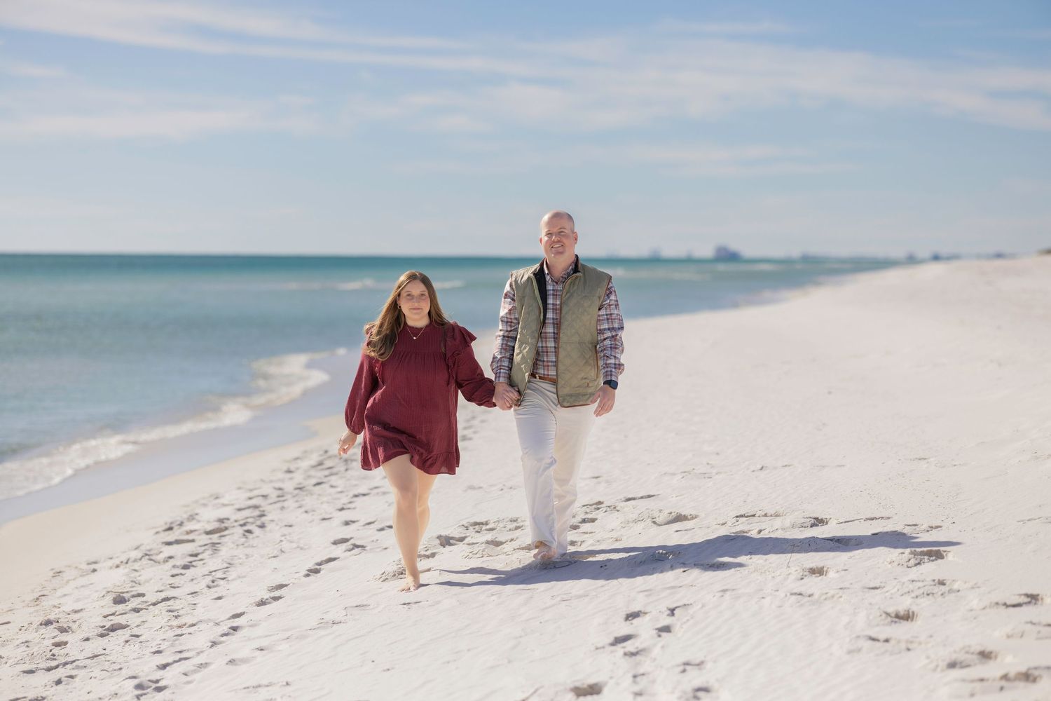 People walking along a pristine white sand beach on a sunny day with clear blue skies and ocean views.