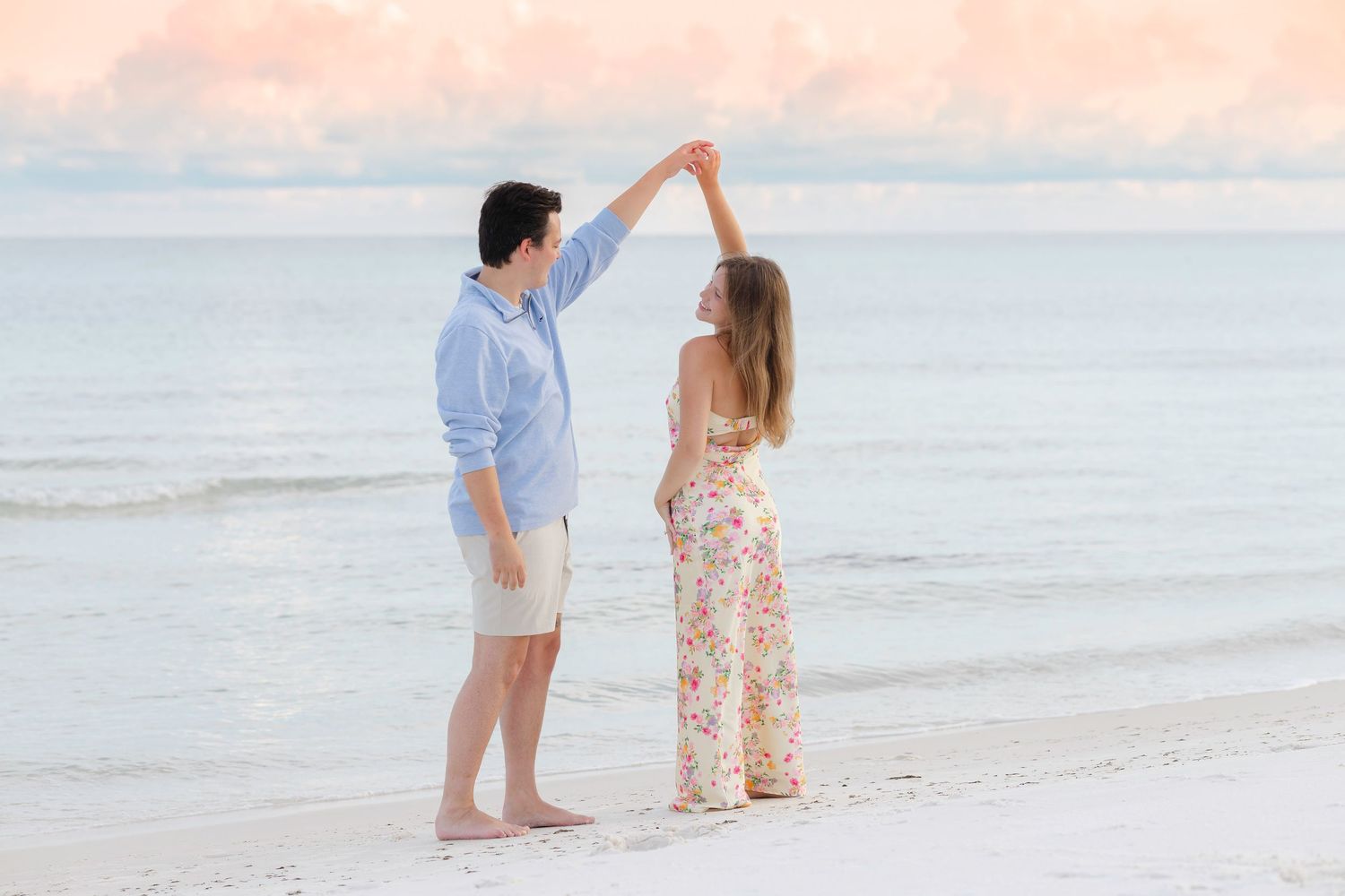 Couple dancing together on a sandy beach at sunset near the ocean.