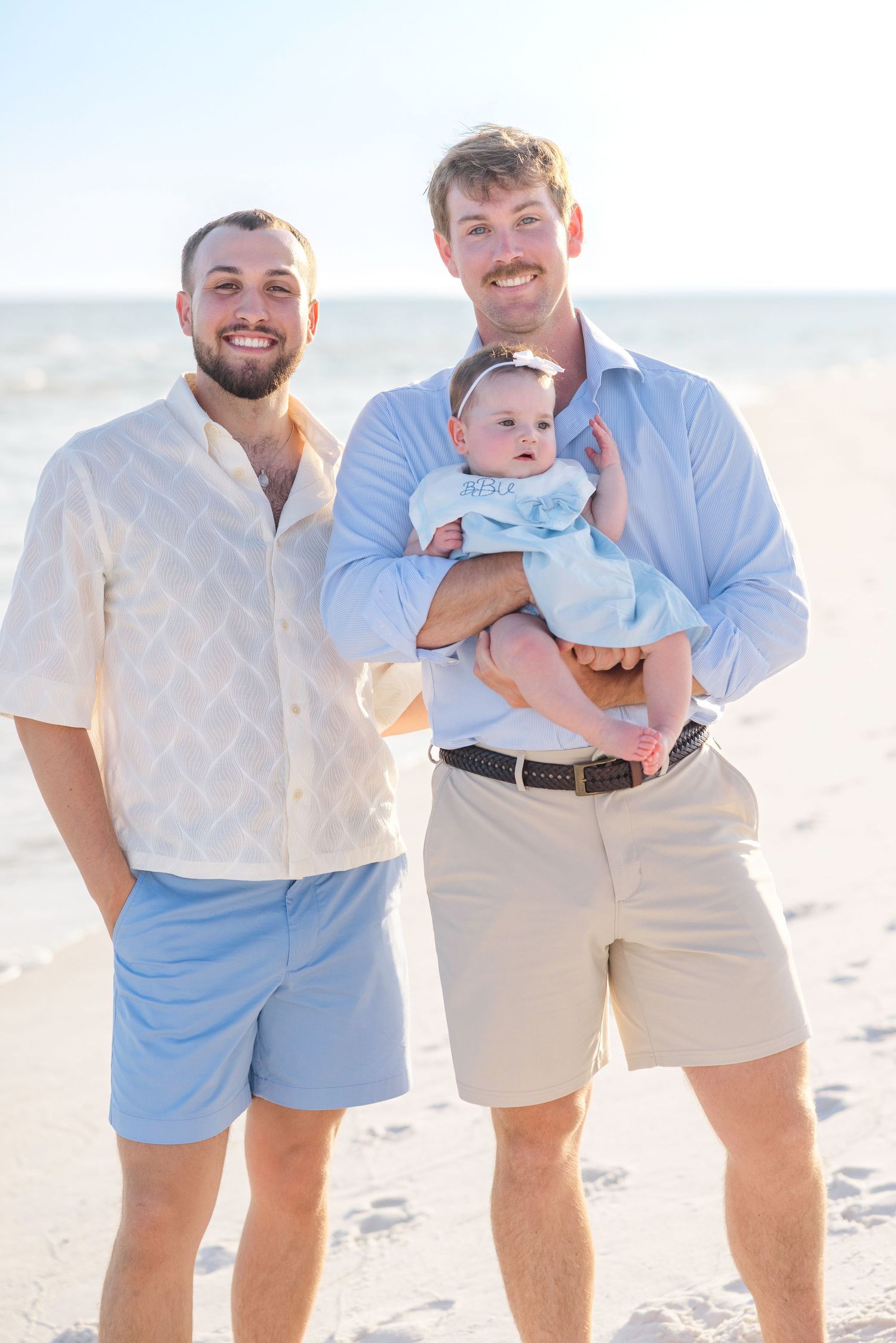 Family members in matching light blue and khaki outfits pose together at the beach during sunset.