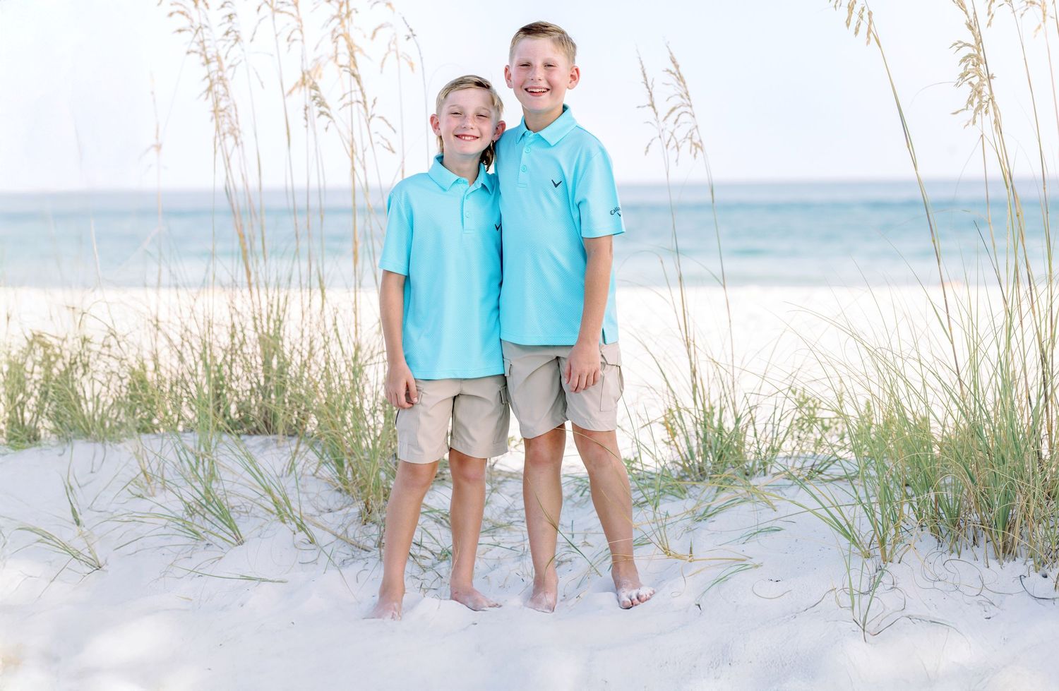 A beach photo shoot shows people in coordinating turquoise and white outfits posing on white sand dunes.