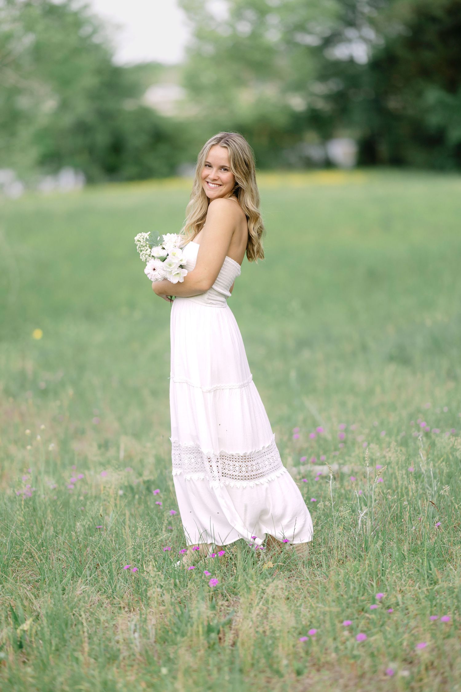 A person in a flowing white dress twirls playfully in a sunlit meadow filled with wildflowers.