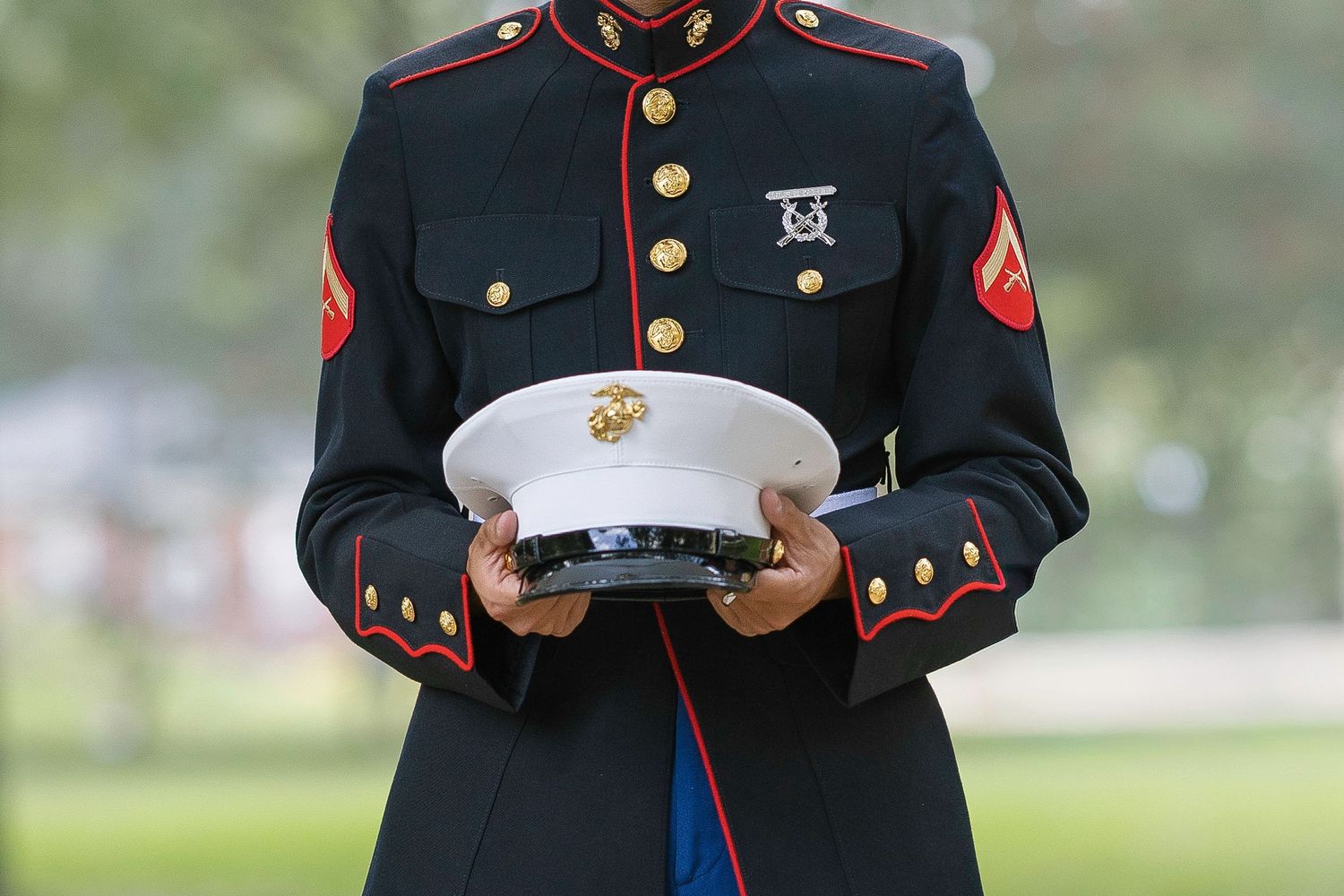 US Marine in dress blues uniform holding white cover cap at formal military ceremony outdoors.