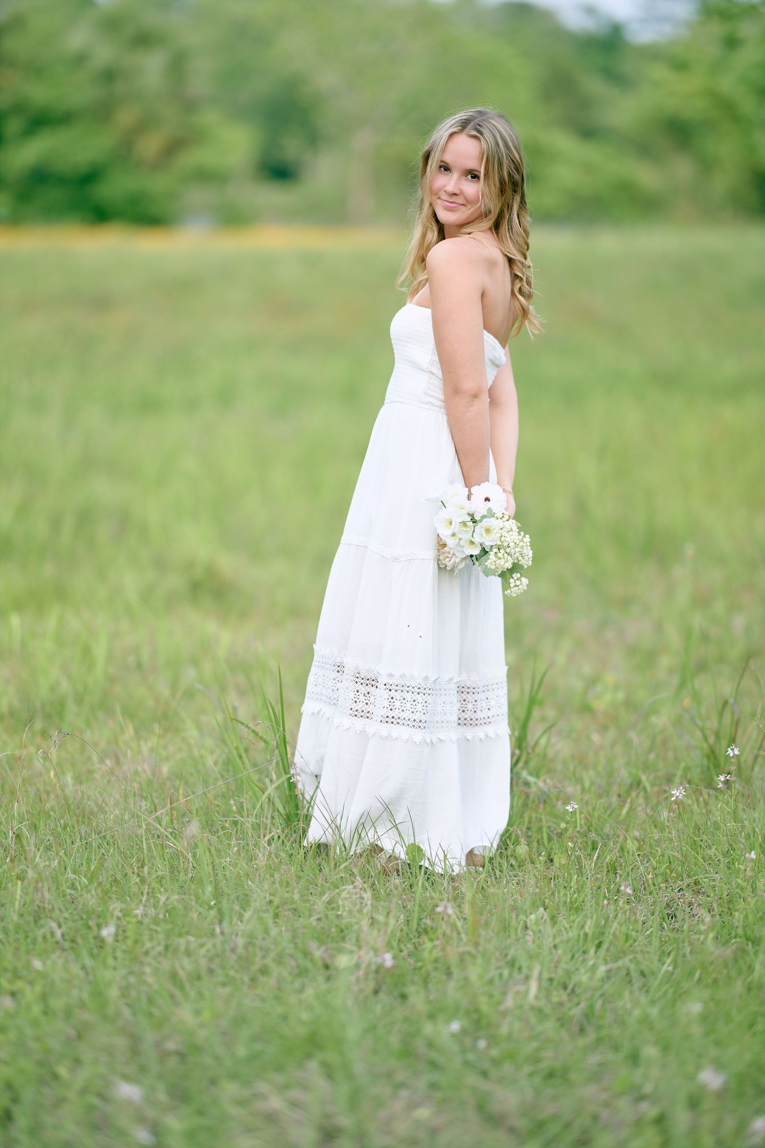Side profile portrait in white lace dress standing in summer meadow.