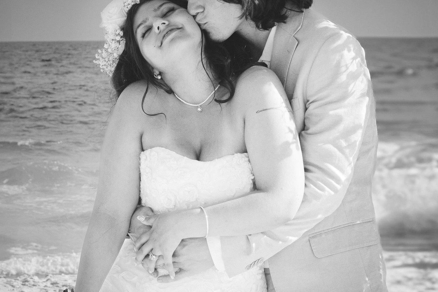 Romantic beach wedding moment captured in black and white with gentle embrace.