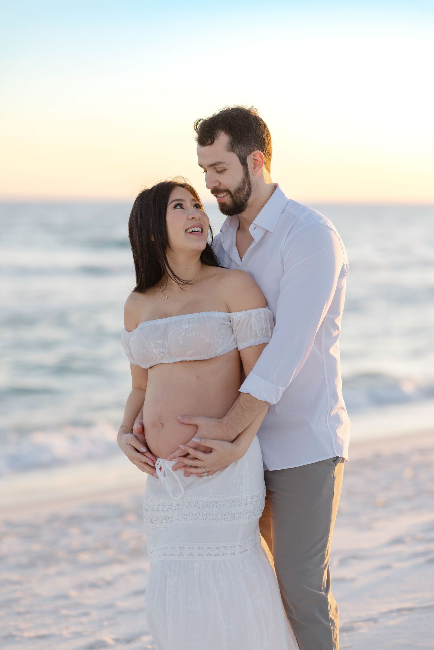 Intimate beach maternity photos of couple embracing on sandy shore during golden hour.