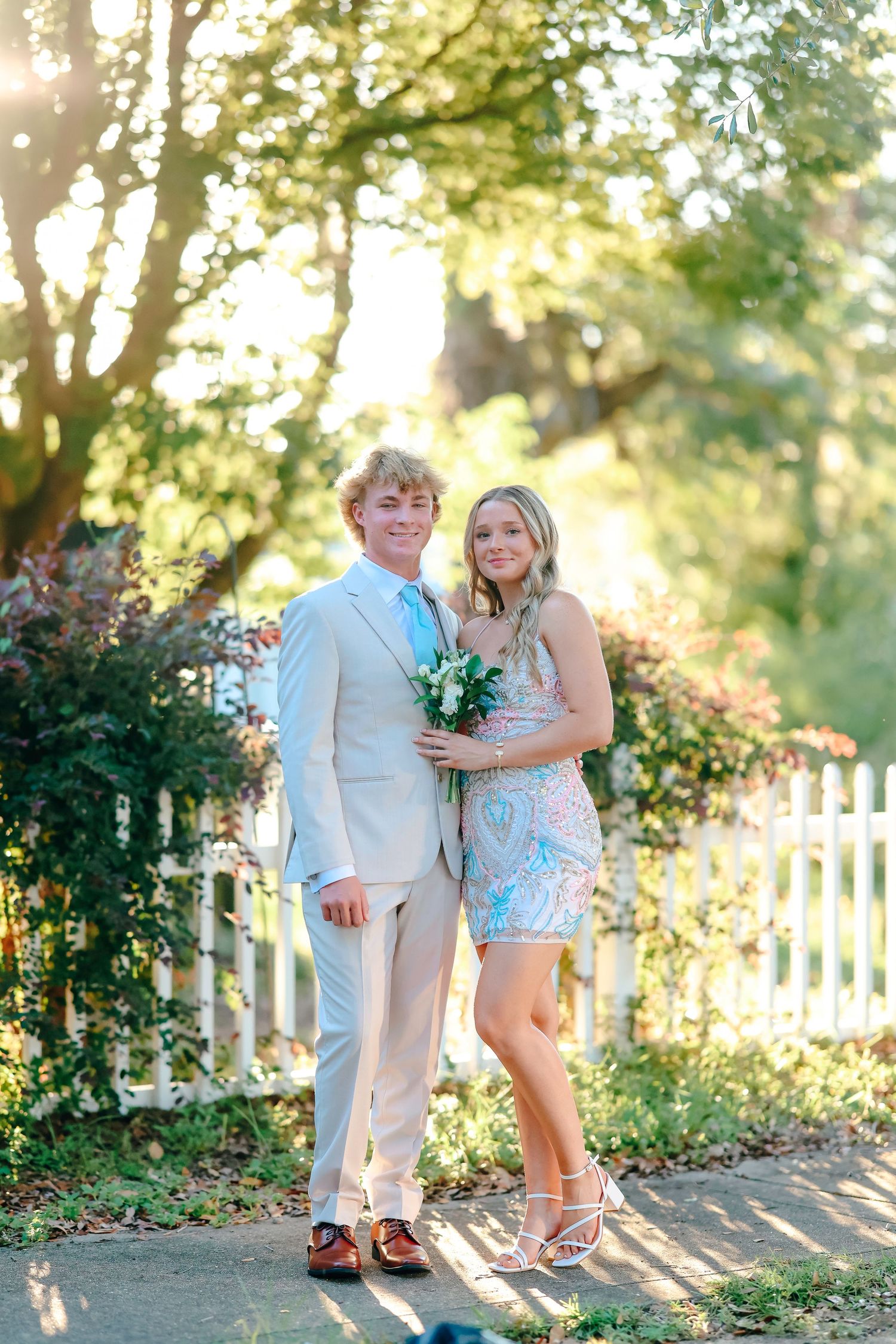 Couple enjoys golden hour photoshoot in garden setting with white picket fence and natural lighting.