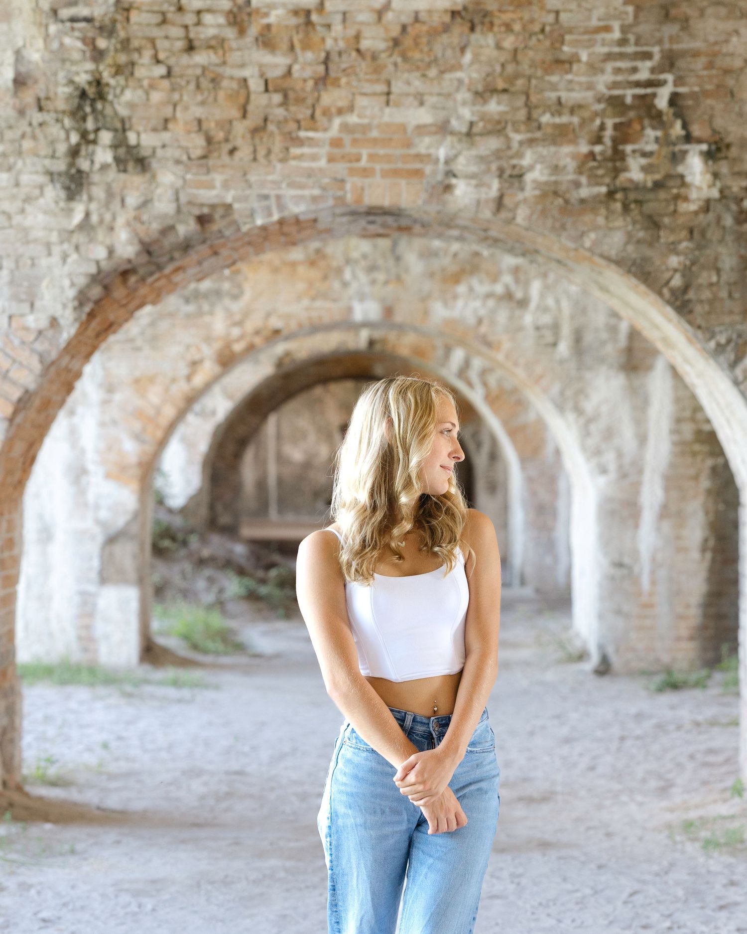 Woman in white top and jeans laughing and striking casual poses in front of an arched stone hallway.