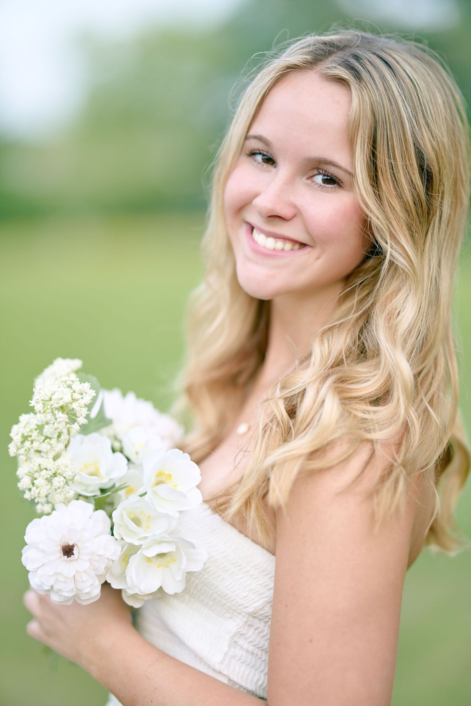 Close up portrait of woman holding white bouquet in sunlit field.