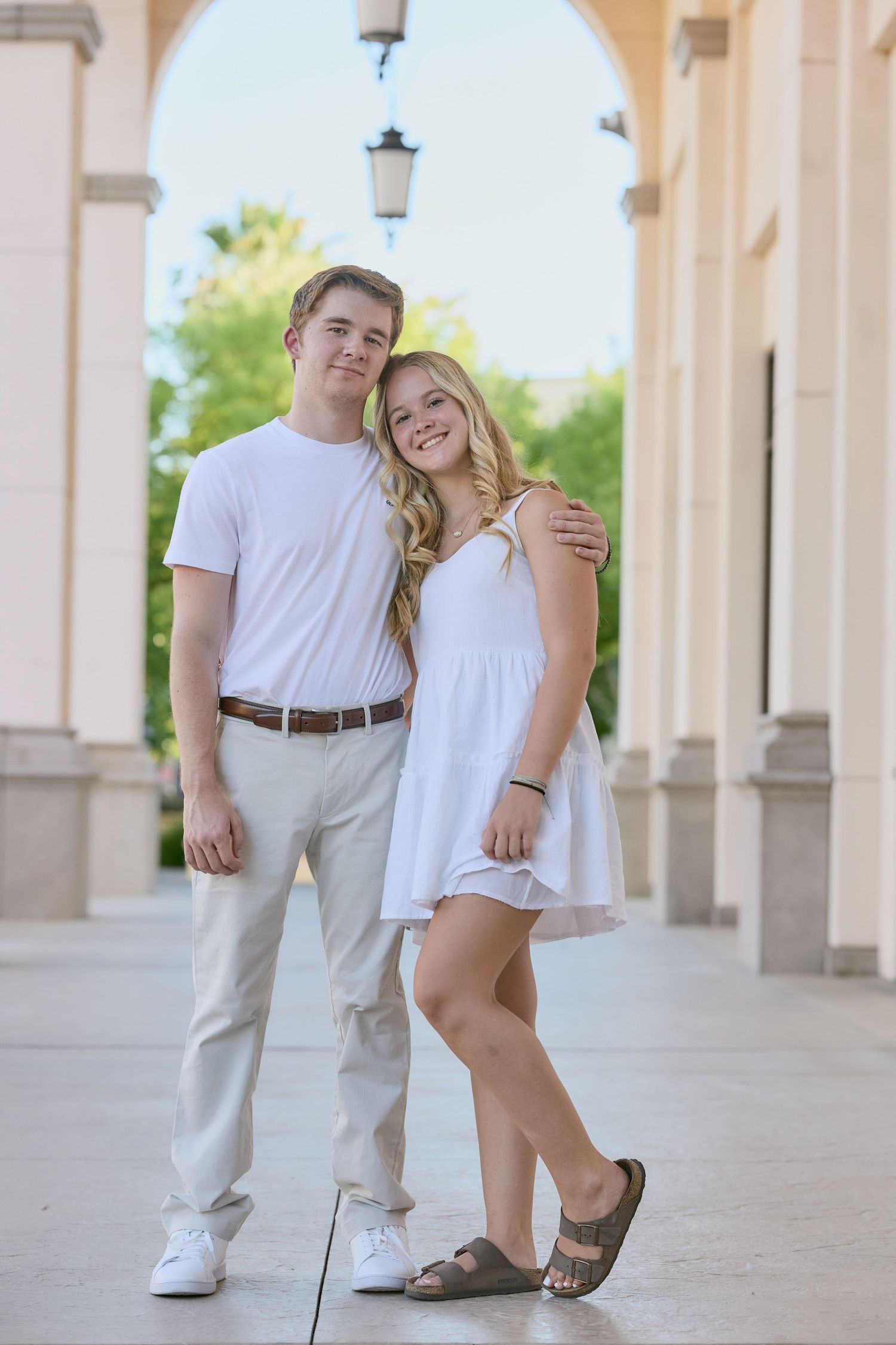 A couple in casual white outfits poses playfully in a series of photos along a columned walkway.