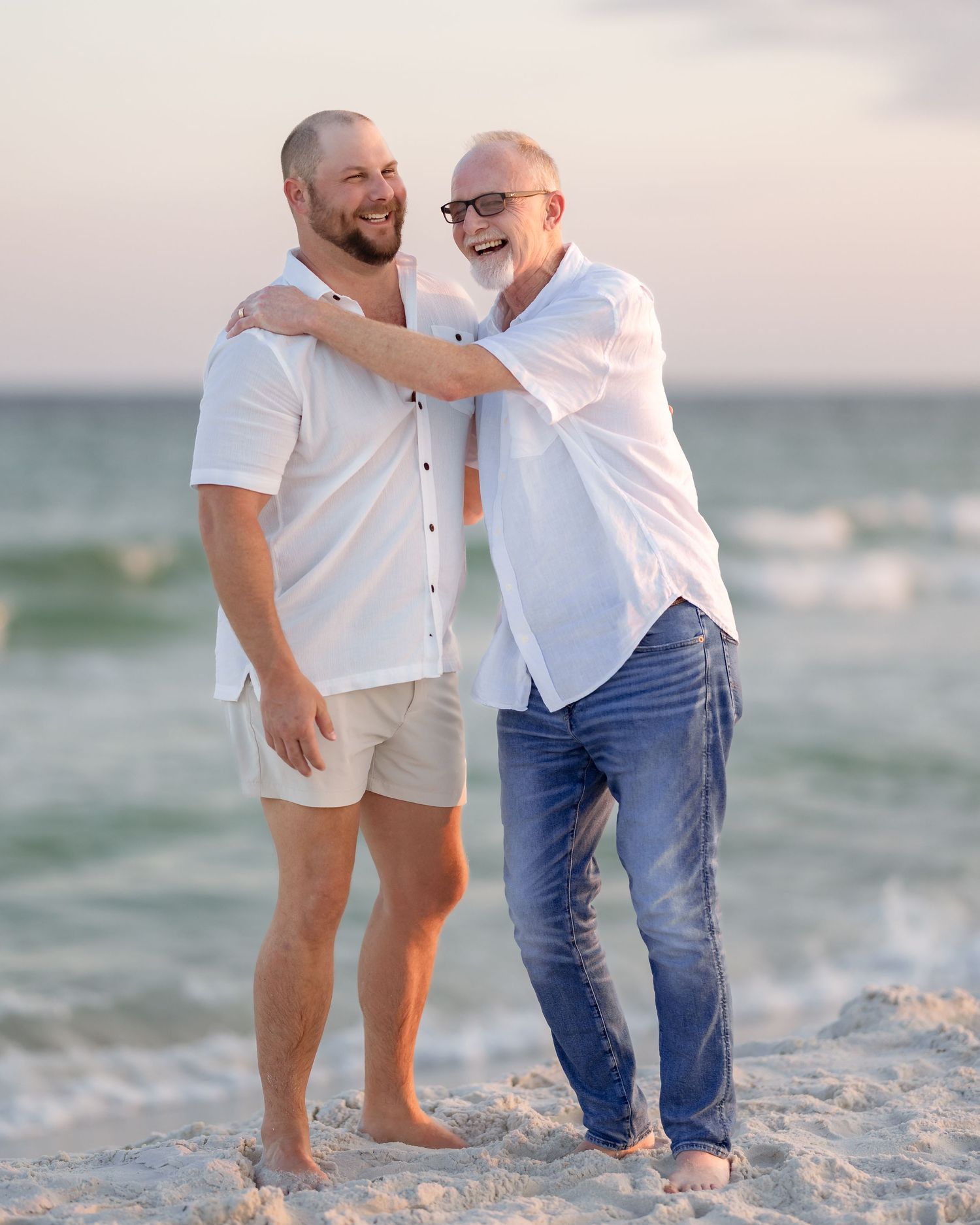 Two men laughing and embracing joyfully together on a sunny beach.