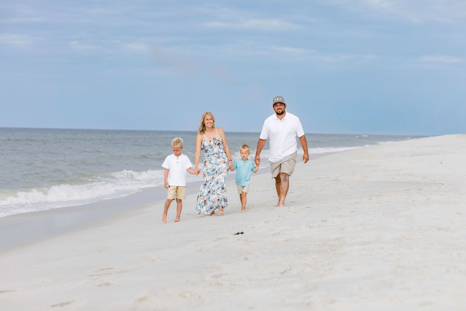 Family of four walking on a white sandy beach near ocean waves on a sunny day.
