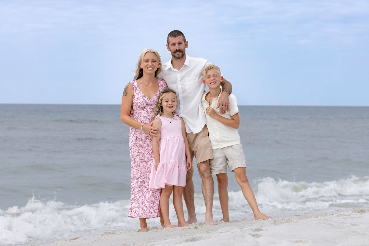 Family of four standing at ocean shoreline, parents with two children smiling at camera.