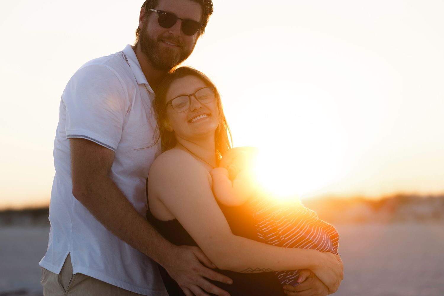 Couple embracing on beach at sunset with warm golden backlight behind them.