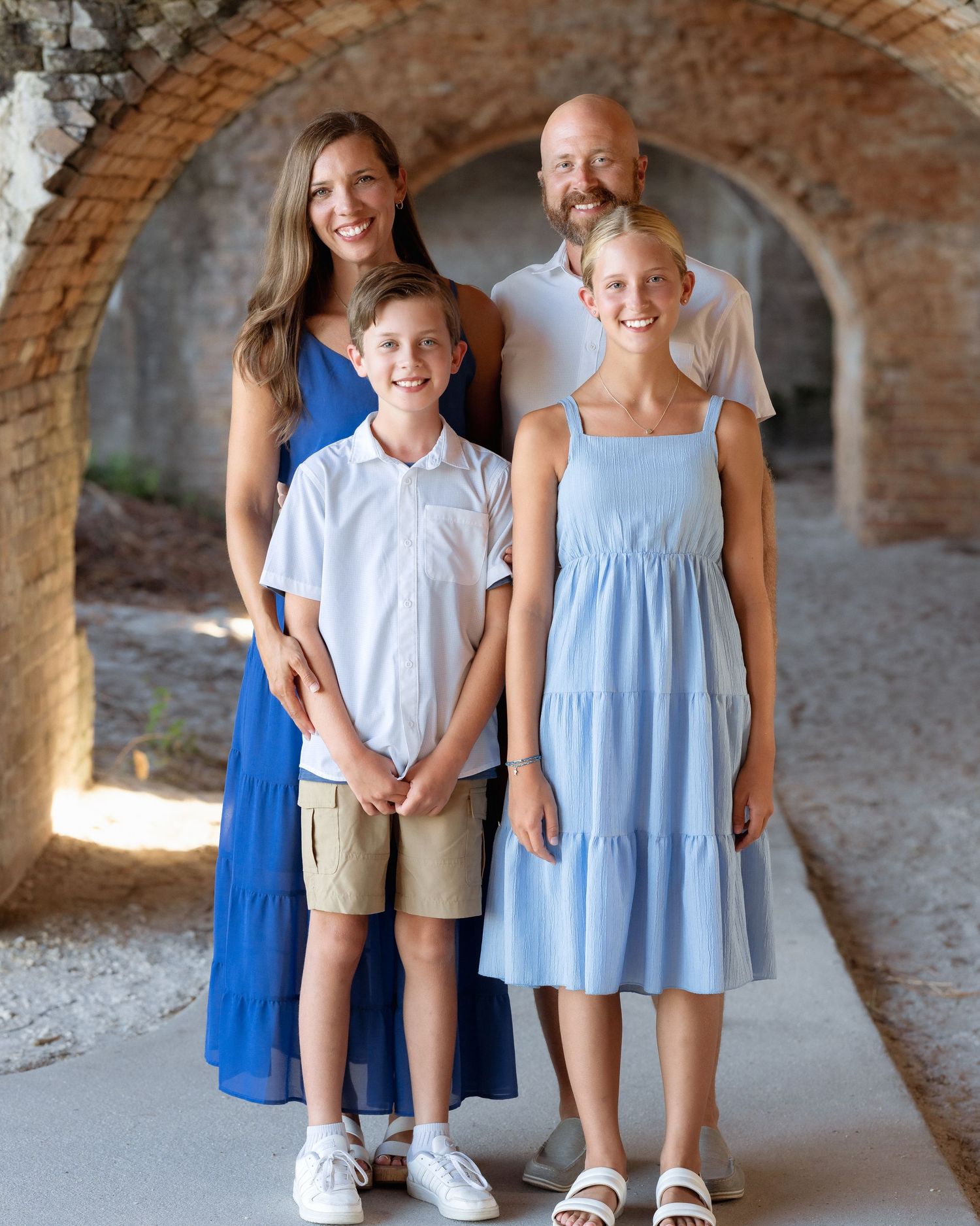 Family of four posing under stone arches, wearing coordinated blue and white outfits, smiling at camera.