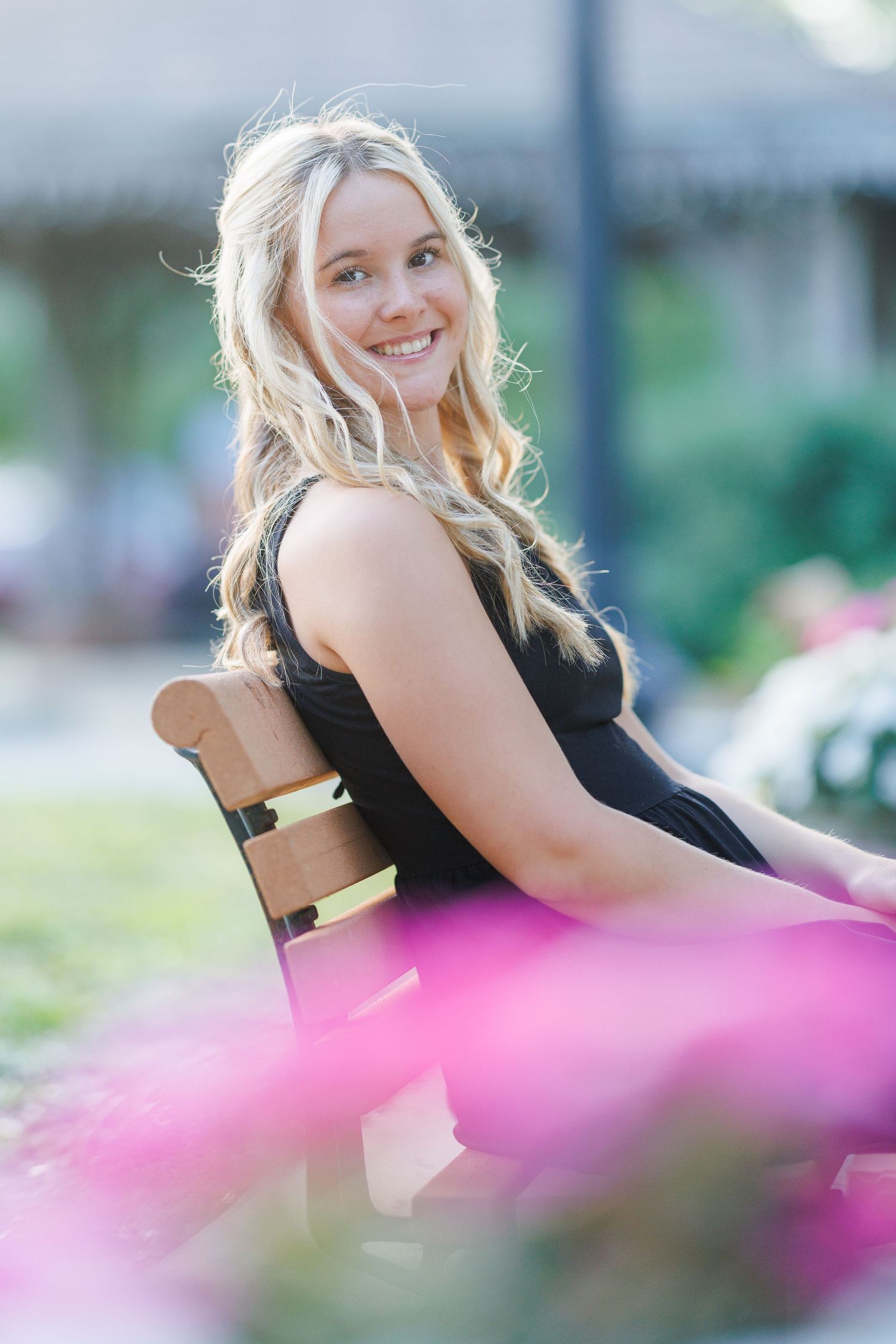 Outdoor portrait featuring pink flowers in the foreground and natural bokeh background effects.