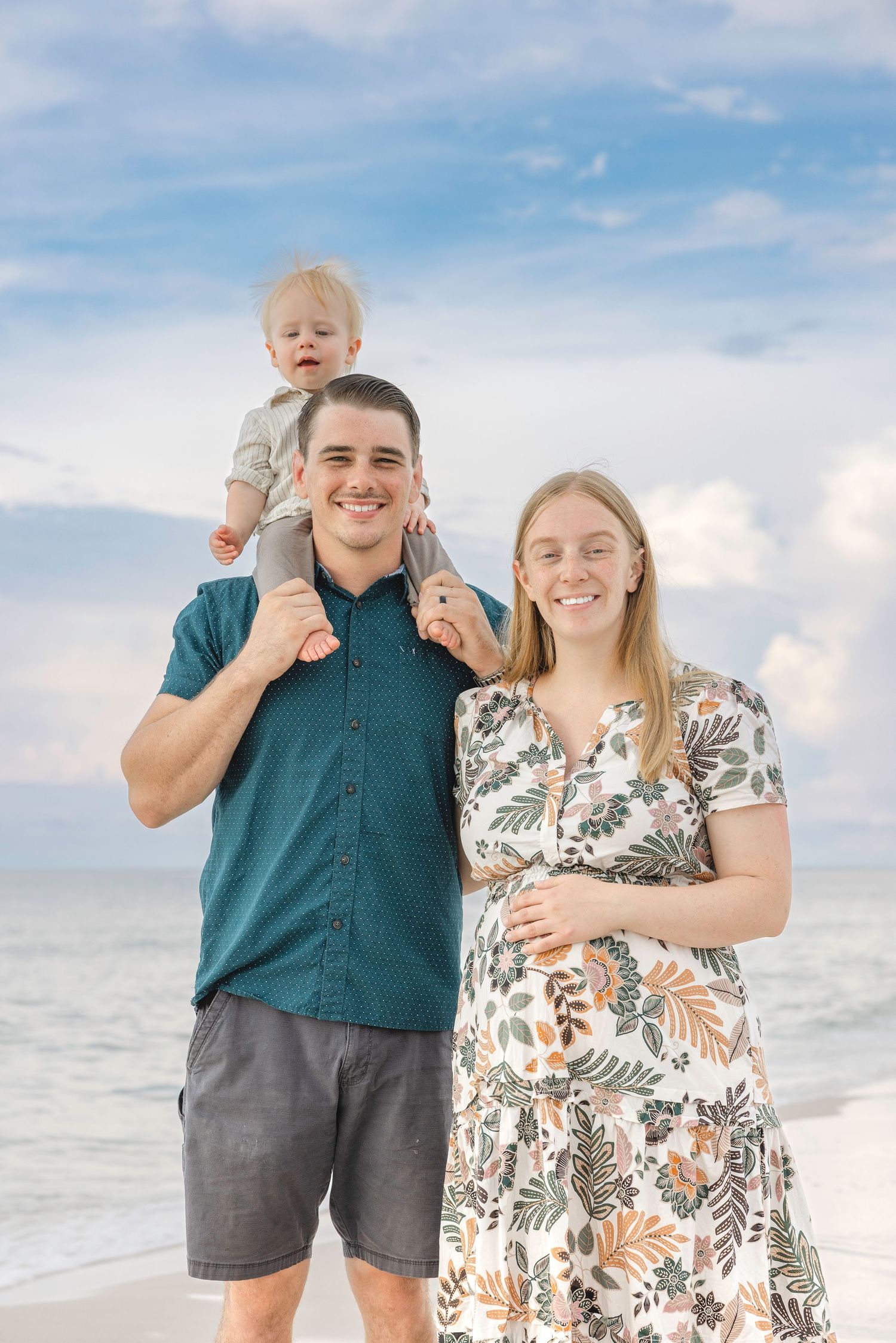 A happy family poses together on a sunny beach while standing near the ocean on a bright day.
