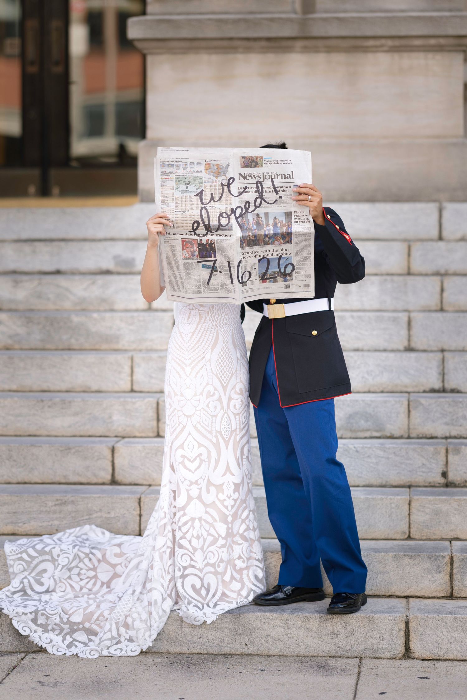 Newlyweds holding newspaper reading 'We eloped 7/16/26', bride in lace gown, groom in Marine dress uniform.