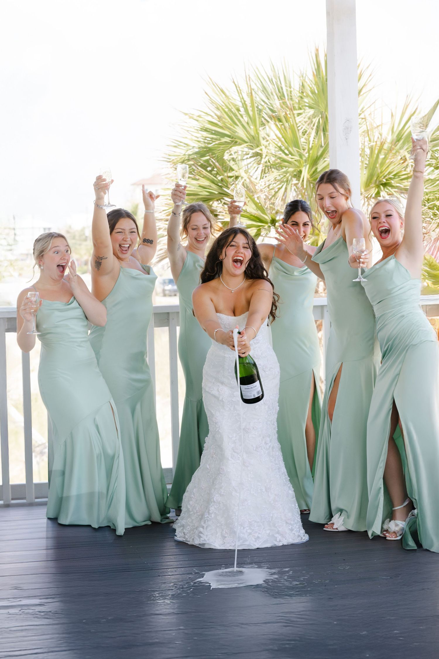 Wedding party in mint green dresses celebrating joyfully on a covered porch.