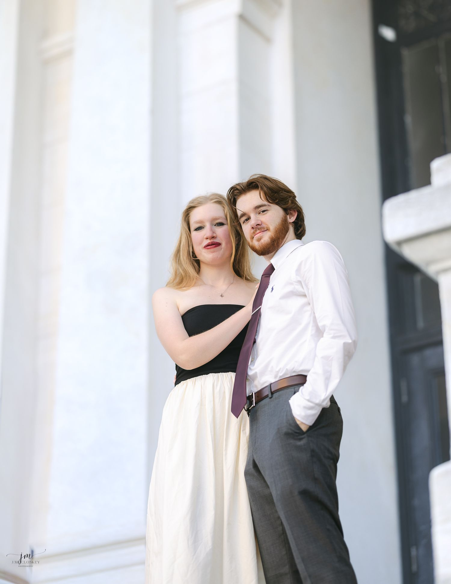A couple poses against white columns in formal attire with dramatic lighting.