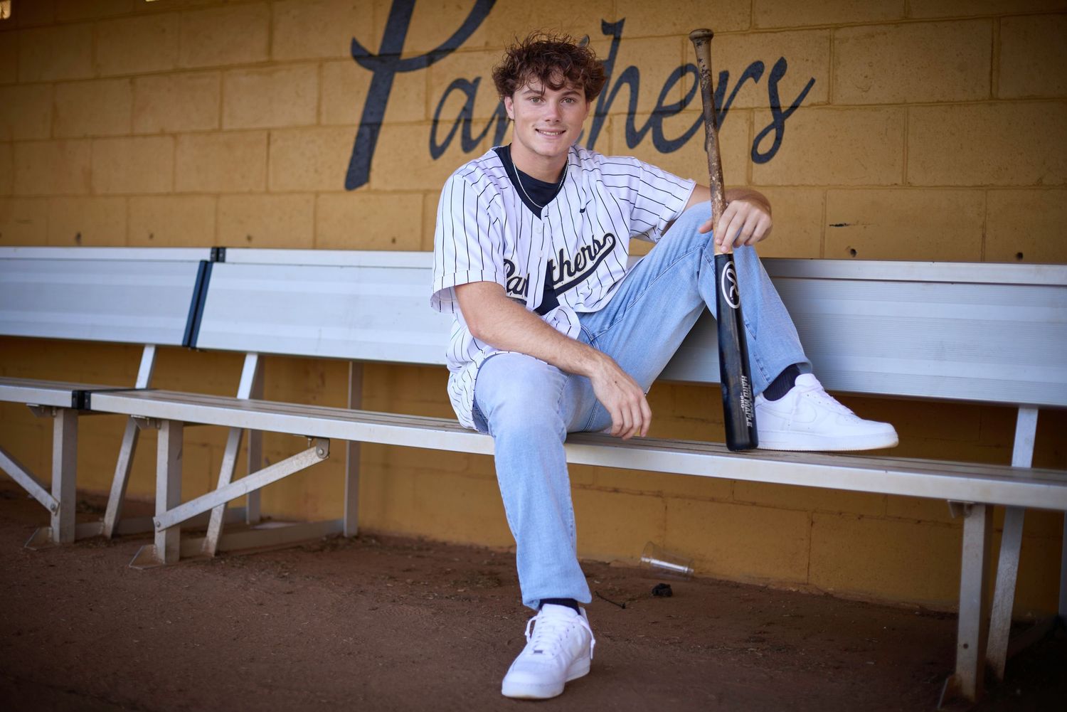 Baseball player in uniform sits casually on dugout bench.