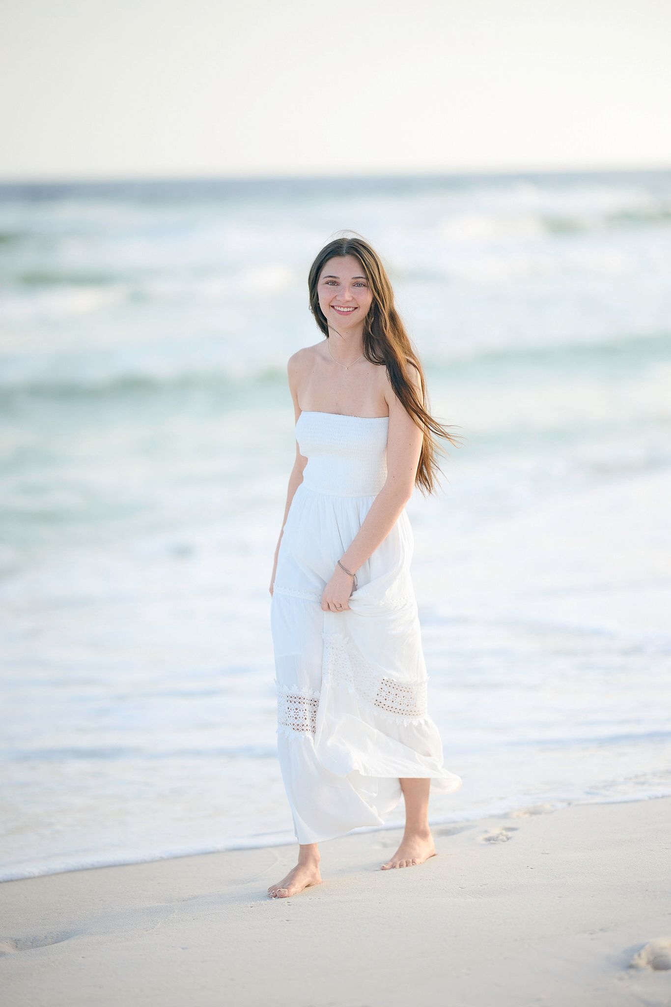 Dreamy beachside photography with flowing white dress and ocean waves in background.