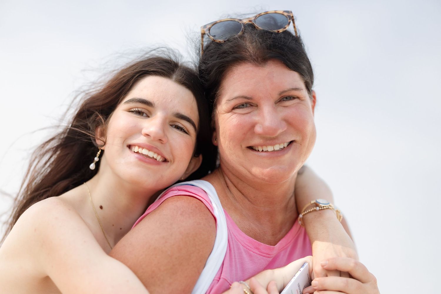 Two smiling women, mother and daughter, posing together outdoors on a bright sunny day.