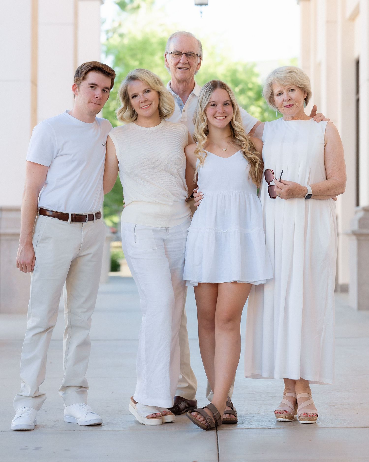 Family of five posing together in white and cream outfits near columns.