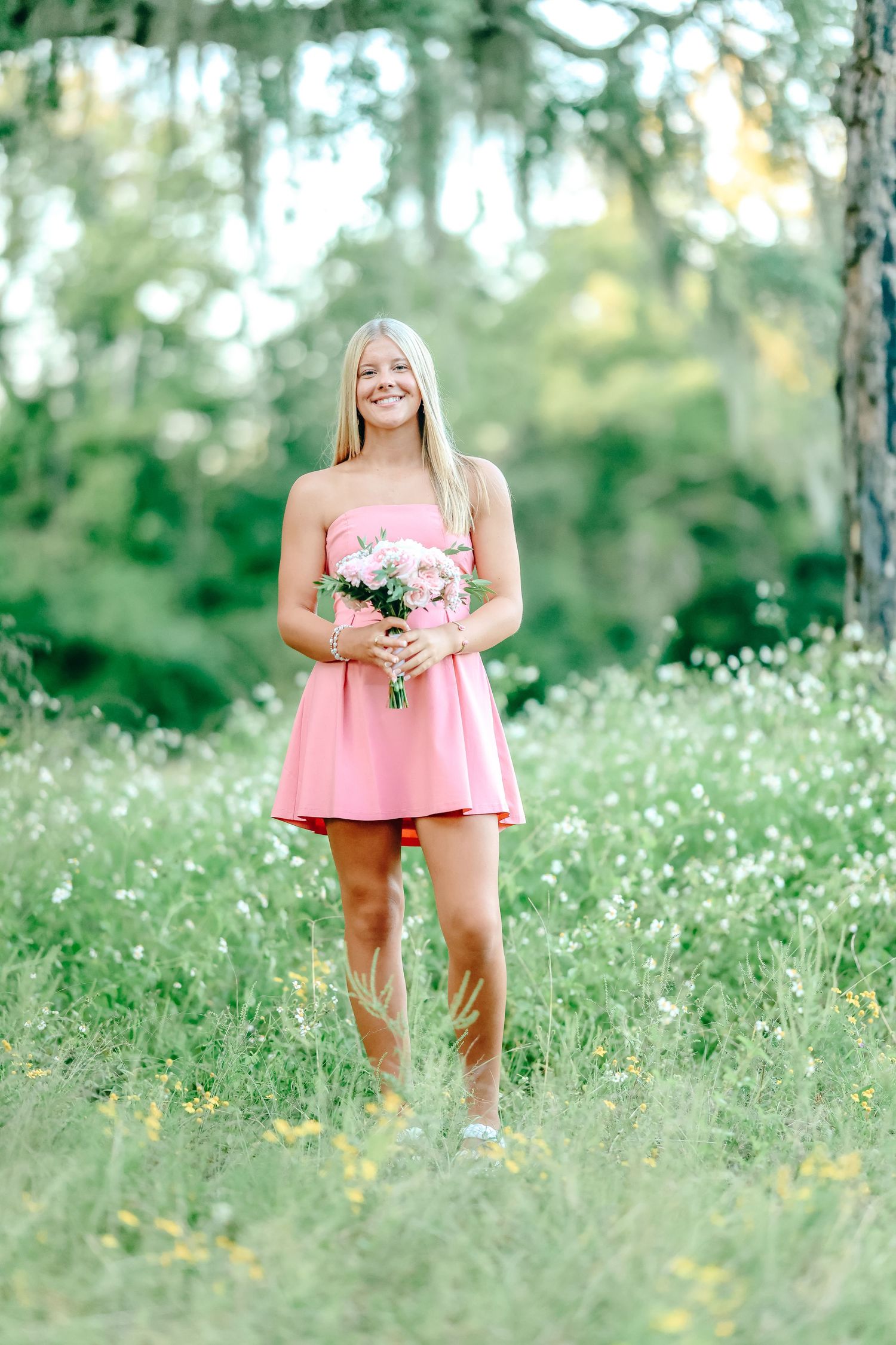 A figure in a pink dress stands in a sun-dappled meadow filled with delicate white wildflowers on a summer day.